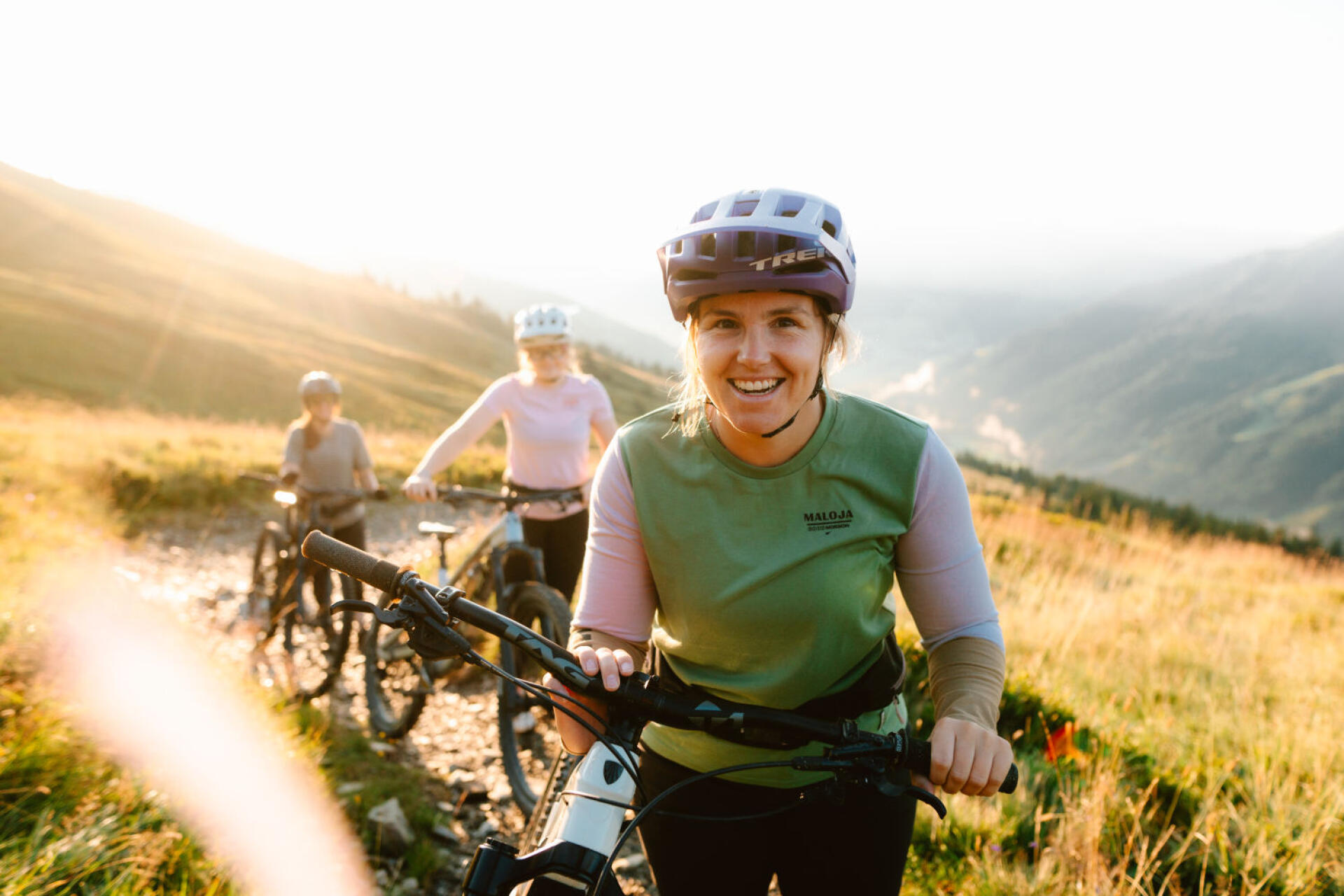 A female biker smiles at the camera, behind her you can see two other women with bikes.
