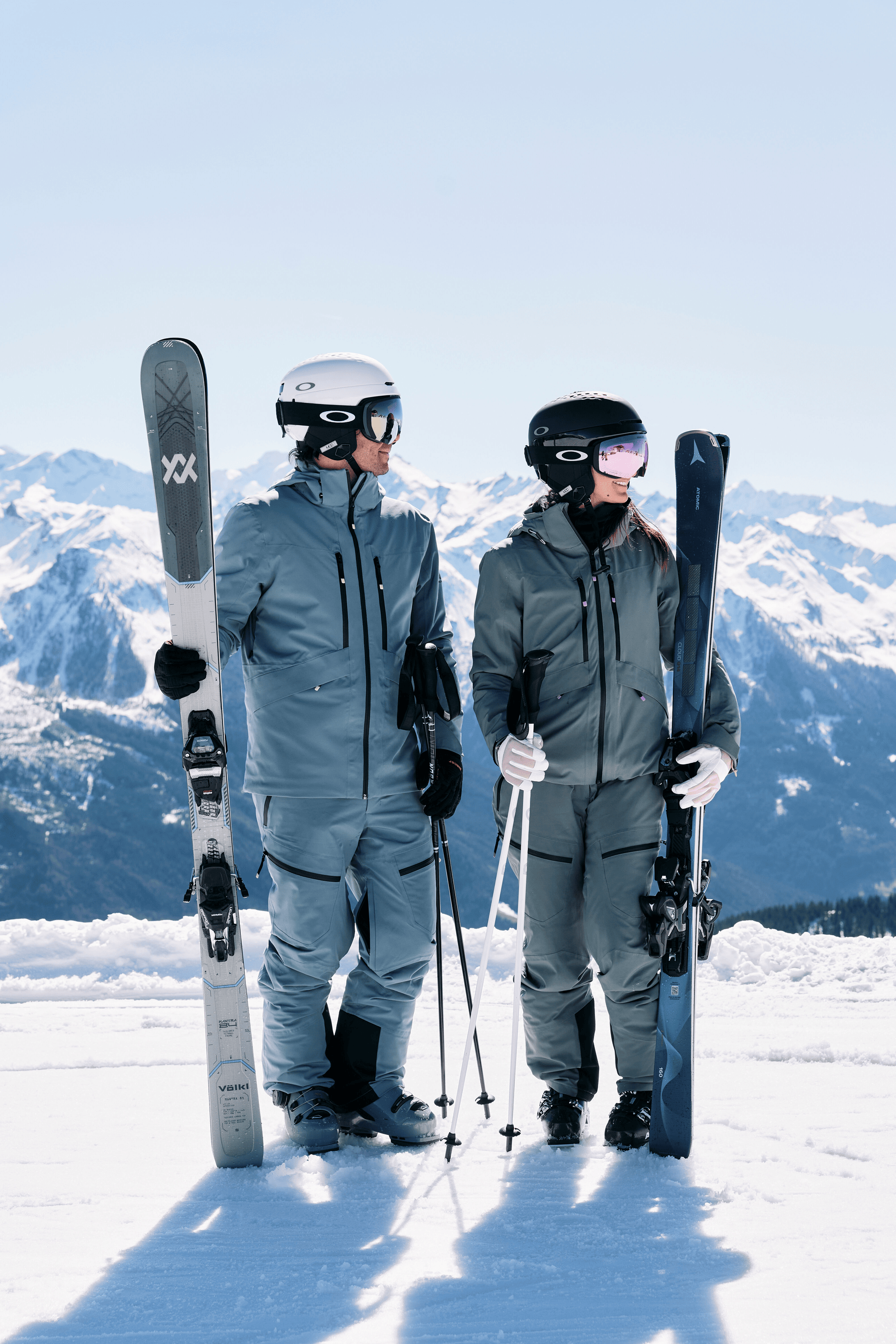 Two skiers in blue clothing standing holding their skis in their hands
