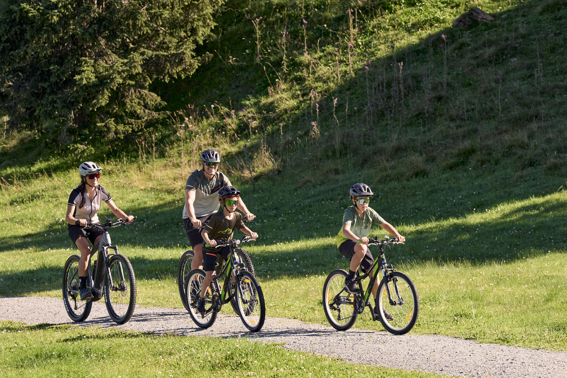 3 bikers ride down a bike trail. It is sunset, casting a warm glow over the landscape