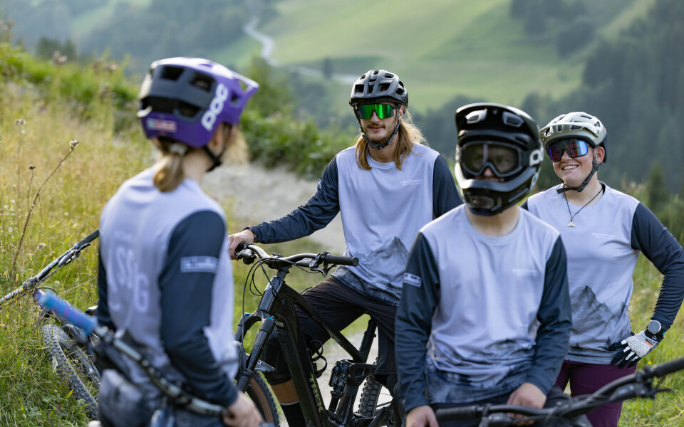 Bike fährt in einer Kurve den Bike-Trail hinunter, im Hintergrund sieht man die Berglandschaft