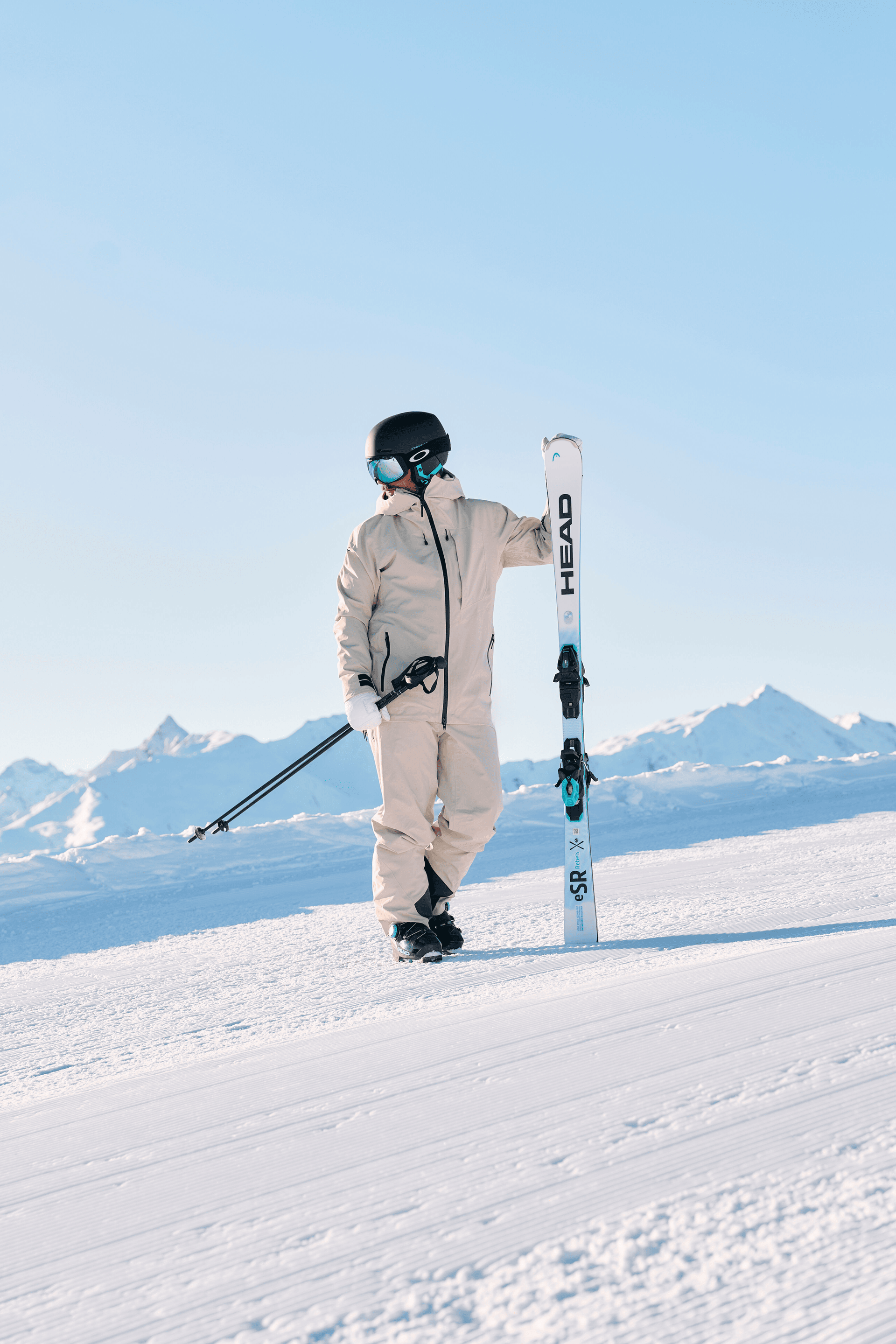Skier in grey clothing standing on the slopes holding a Head ski in his hand