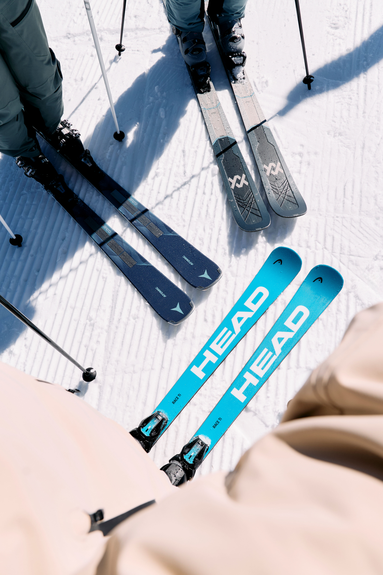 Close-up of three pairs of skis in the snow. Brands are Völkl, Atomic and Head.