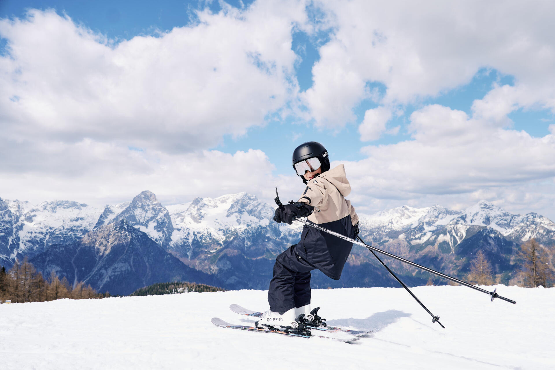 A child stands on the slope with snow-covered mountains in the background