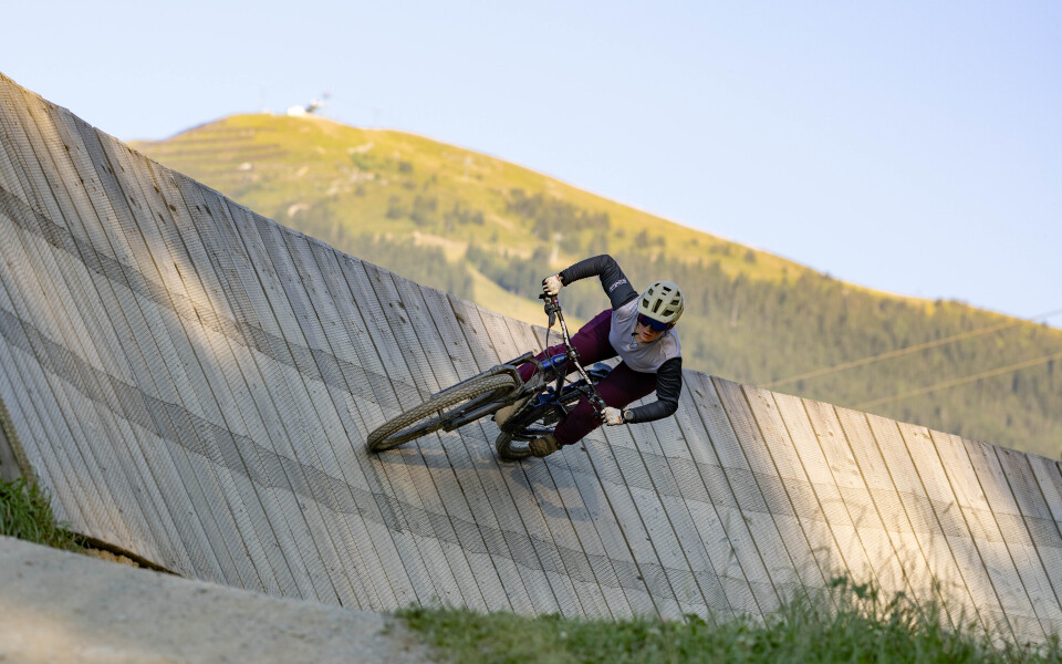 Mountainbiker fährt dynamisch durch eine Steilkurve auf einem Bikepark-Trail in den Bergen bei sonnigen Bedingungen