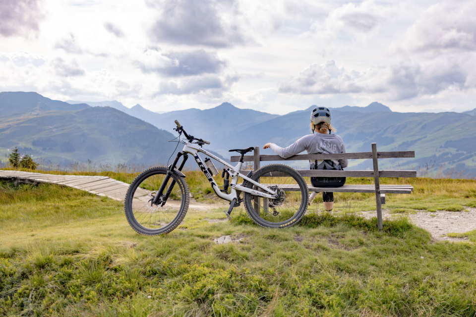 Eine Frau sitzt auf einer Sitzbank, das Bike ist an der Bank angelehnt.