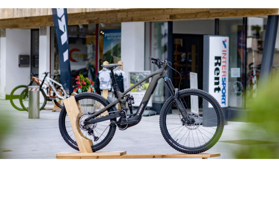 Ein elegantes schwarzes Mountainbike, das auf einem Holzständer vor einem Sportartikelverleih ausgestellt ist und Abenteuerlust und Outdoor-Begeisterung vermittelt.